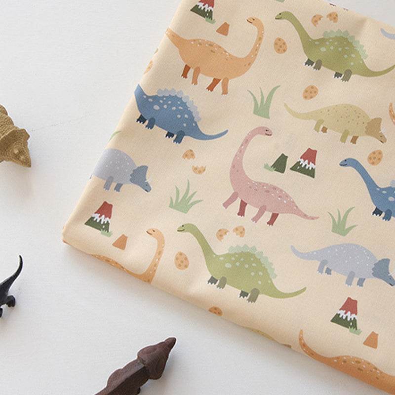 Handmade Printed Fabric in cream cotton with colorful cartoon dinosaurs, scattered eggs and small trees in a playful print