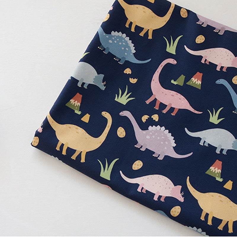 Handmade Printed Fabric in navy cotton with colorful cartoon dinosaurs, eggs and small grassy accents in a playful repeating pattern