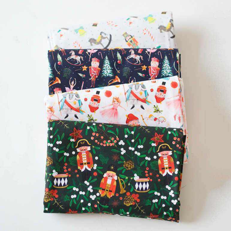Printed Nutcracker Fabric shown as folded cotton panels in white, navy, pink and green with colorful holiday character prints