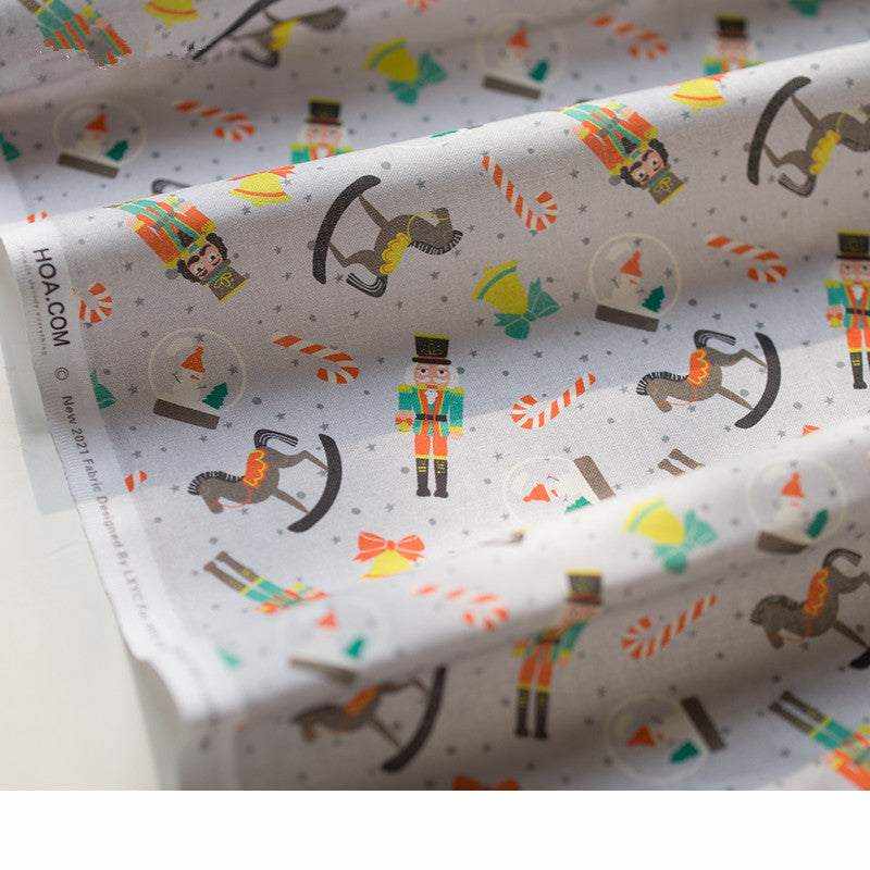 Printed Nutcracker Fabric in light gray cotton, patterned with colorful toy soldiers, rocking horses, drums and festive motifs.